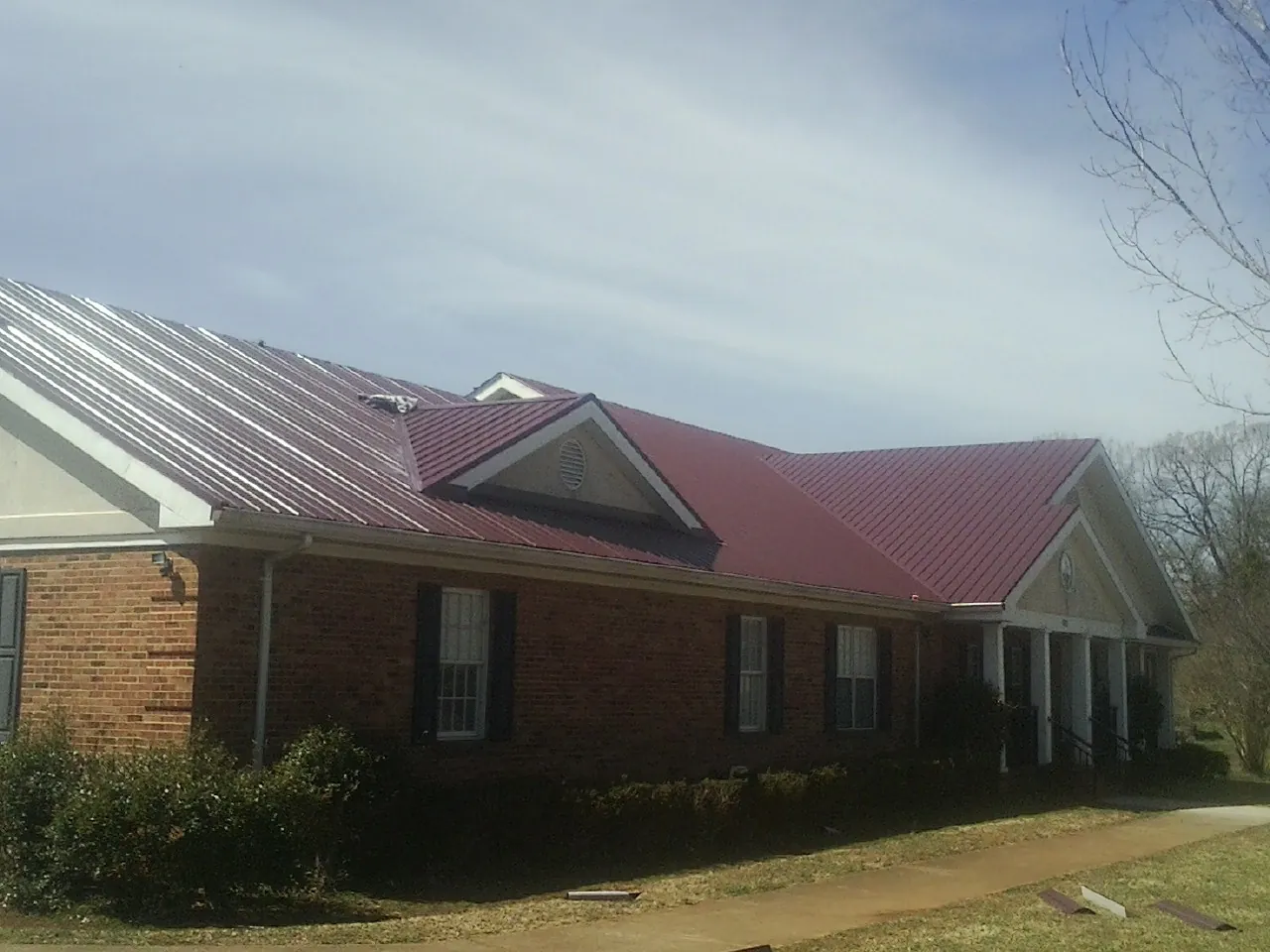 Red metal roof with gabled entries on a long brick building, from a Hail Damage Roof Repair job in Woodbury Heights