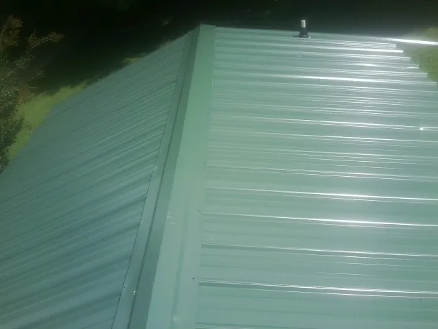 New green metal panels meeting at the ridge of a roof — Flat Roof Repair work by our crew in Woodbury Heights