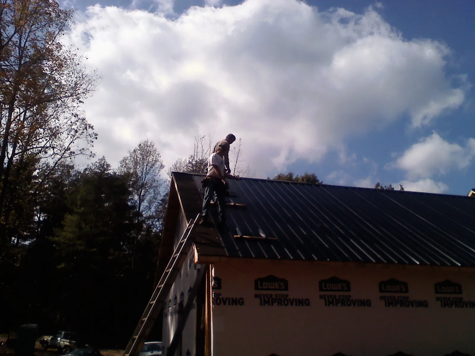 Roofer fastening dark metal panels high against a cloudy sky, from a Roof Inspection job in Woodbury Heights