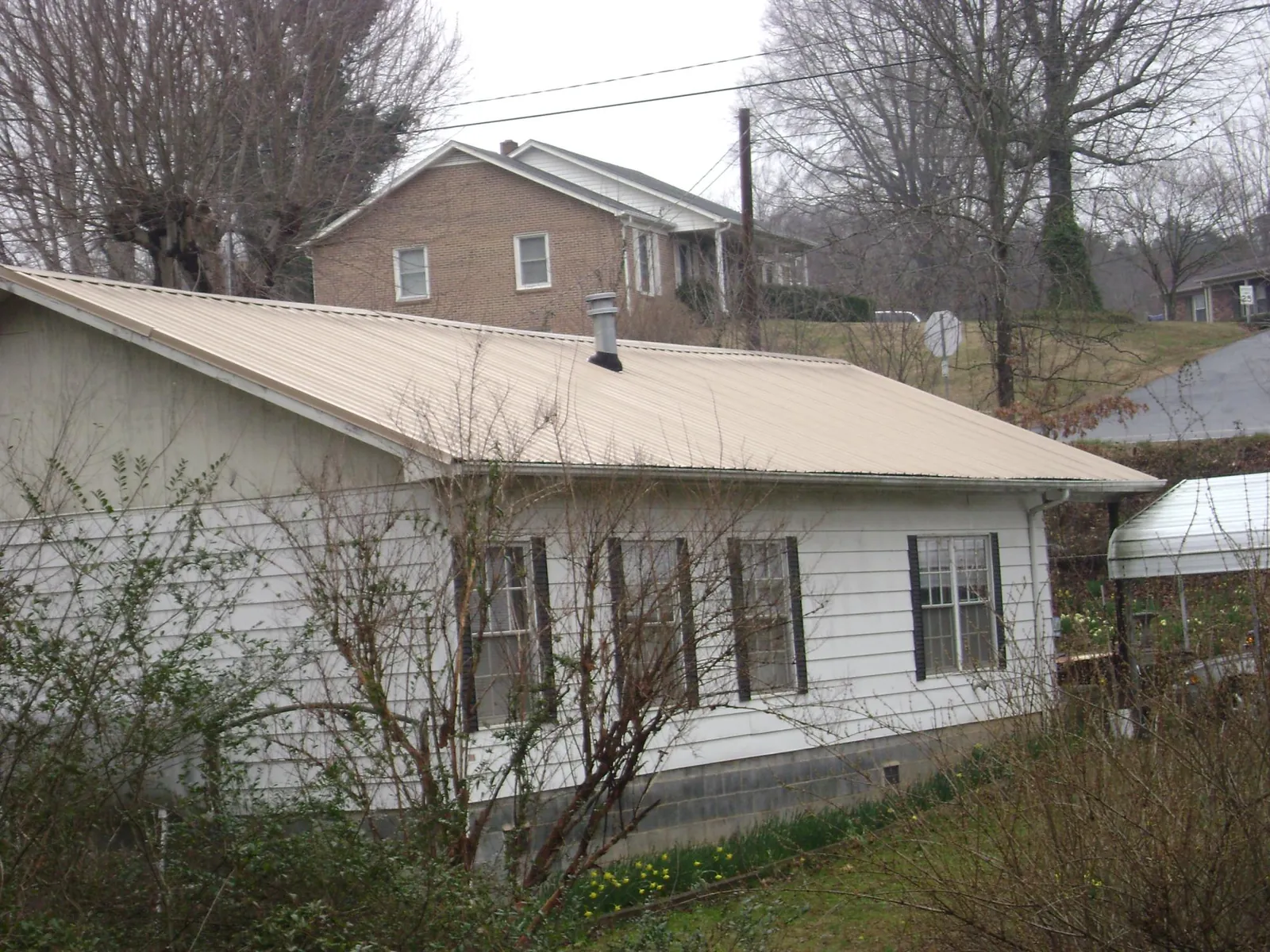 Tan metal roof on a white sided house set into a hillside — Commercial Roofing by Roofing Brothers in Woodbury Heights
